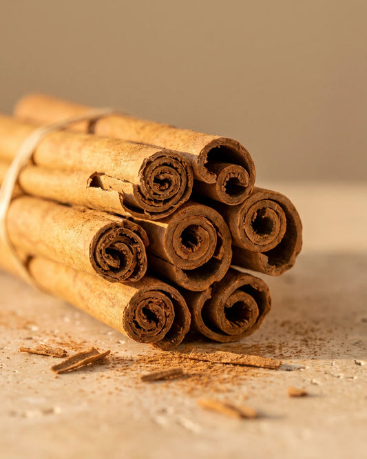 A bundle of cinnamon quills with a dusting of ground cinnamon on travertine — the sweet, warm spice scent of Delune Cinnamon Pure Essential Oil